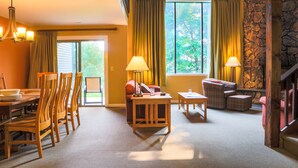 A room with a dining table, chairs, a sofa, a small table with a lamp, and a stone wall. - Cascade Lodge u31 - Short Walk to Main Street! (Lake Placid)