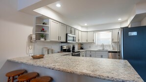 A kitchen with white cabinets, a granite countertop, and wooden stools.