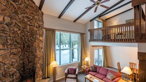 A cozy living room with a stone wall, fireplace, and a balcony with wooden railings.