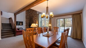 A dining area with a wooden table, chairs, a chandelier, and a stone wall.