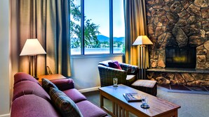 A cozy living room with a stone fireplace, a large window with a view of the outdoors, and a plush red sofa.