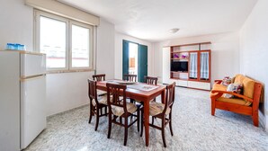 Un coin repas avec une table et des chaises en bois, un canapé, un téléviseur et un réfrigérateur.