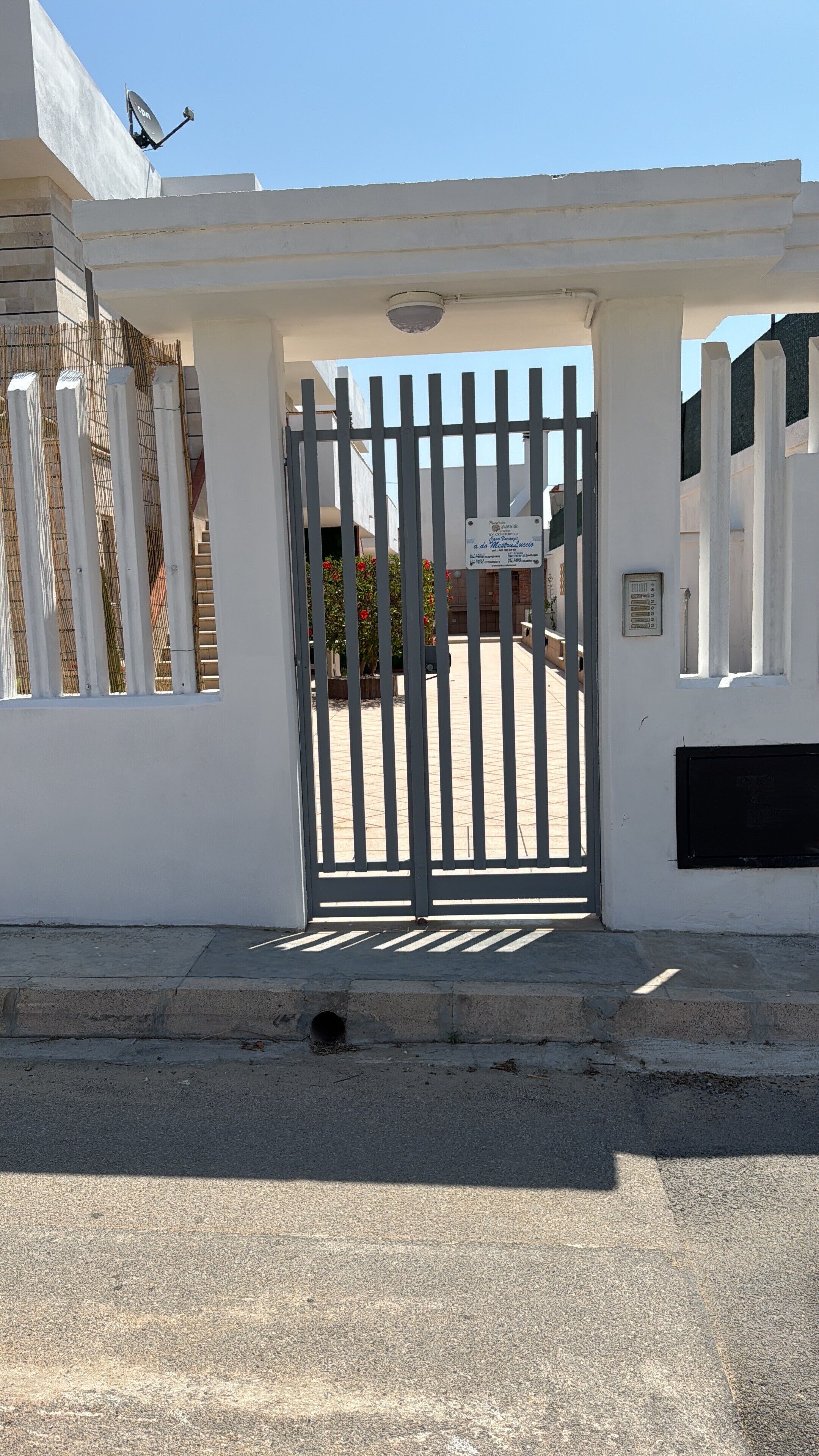 A gated entrance with a sign, a satellite dish, and a building facade.