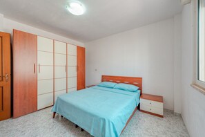 A bedroom with a bed, a nightstand, a wardrobe, and a window.