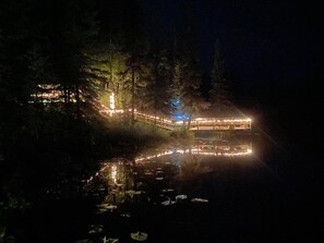 En byggnad vid sjön med upplysta konstruktioner och en spegelbild i vattnet.