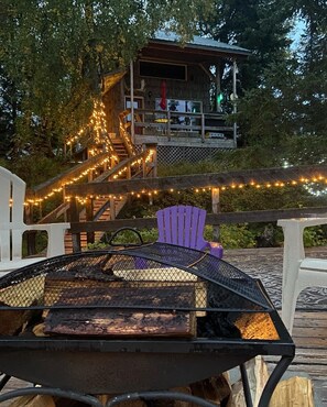 En uteplats med en grill, stolar och utsikt över en byggnad med trappor och ljusslingor.