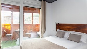 A bedroom with a large bed, wooden headboard, and a sliding glass door leading to an outdoor area with a chair and table. - Steps from Grandvalira  Cozy Ski Haven+Parking

 (Soldeu)