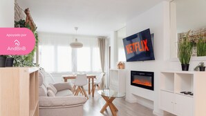 A modern living room with a sofa, dining table, and chairs, a glass coffee table, a fireplace, and a TV mounted on the wall. - Steps from Grandvalira  Cozy Ski Haven+Parking

 (Soldeu)