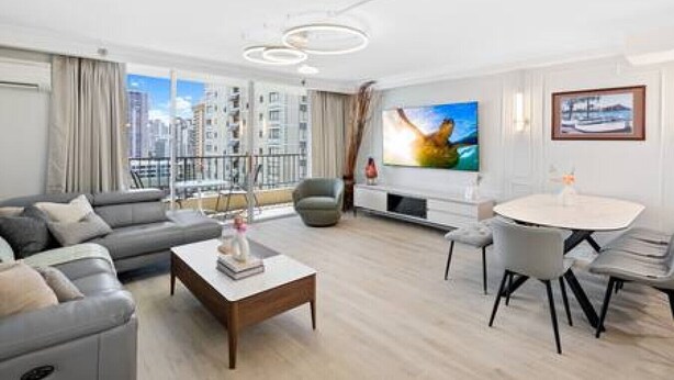 A modern living room with a grey sofa, a coffee table, a TV, and a dining area with chairs.