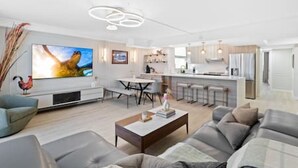 A modern living room with a flat-screen TV, a dining area, and a kitchen with bar stools.