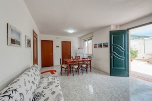 A room with a dining table, chairs, a sofa, and a green door leading outside.