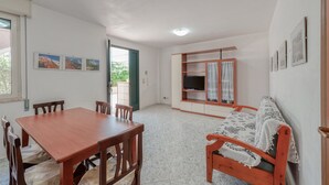 Ein Zimmer mit einem Holzesstisch, Stühlen, einer Couch, einem Fernseher auf einem Holzboden und gerahmten Bildern an der Wand.