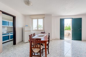 Un coin repas comprenant une table et des chaises, une fenêtre, un réfrigérateur et un espace cuisine avec des placards bleus.