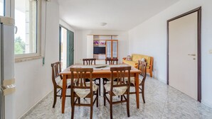 A dining area with a table and chairs, a kitchen in the background, and a door to the right. - Apartment 'Paola' with Private Terrace and Air Conditioning (san pietro in bevagna)