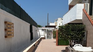 A courtyard with a tiled floor, a wooden bench, a white table with chairs, and a green hedge. - Apartment 'Paola' with Private Terrace and Air Conditioning (san pietro in bevagna)