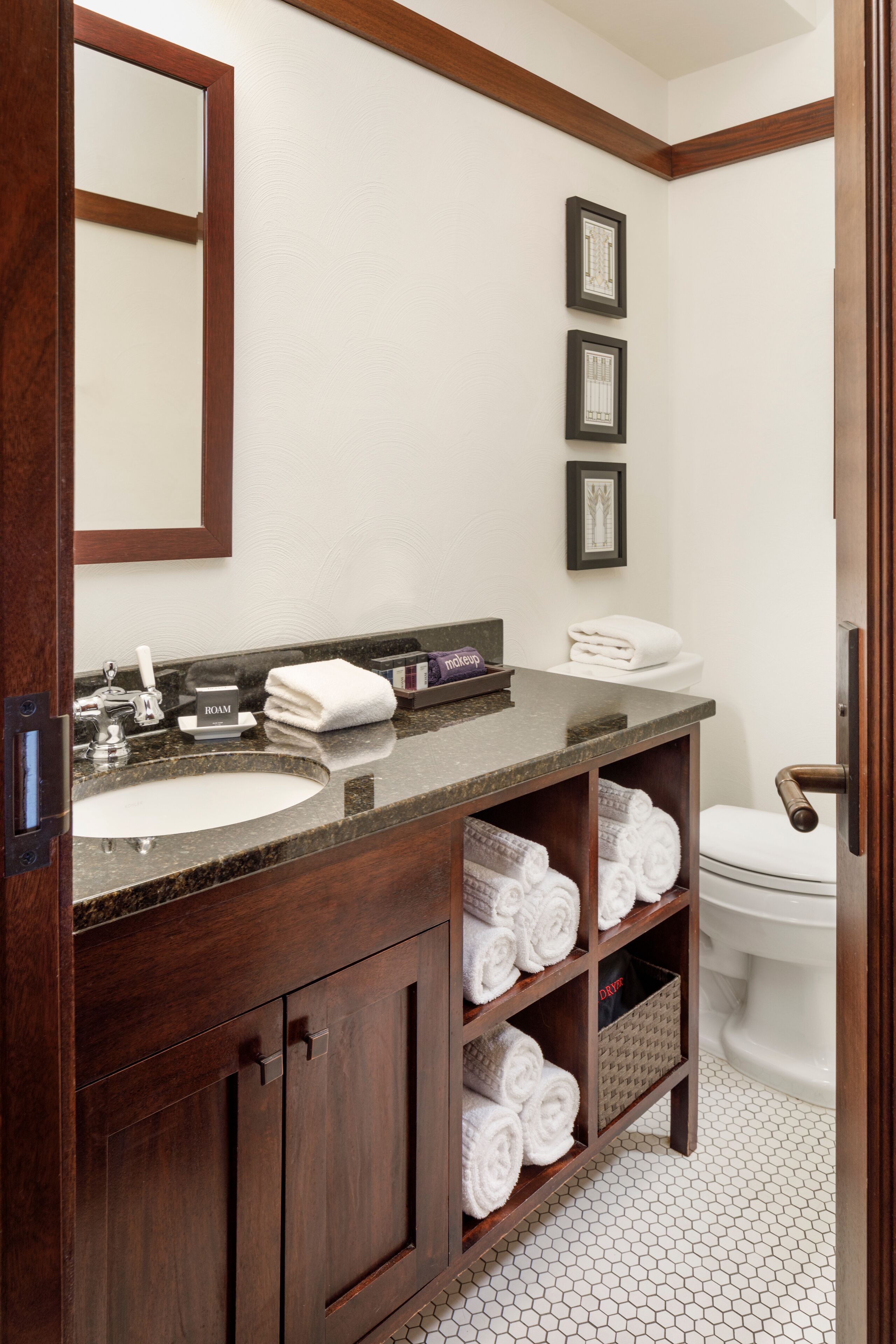 Une salle de bain avec un meuble-lavabo en bois, un évier, un miroir et des toilettes. On y trouve des serviettes et un panier posés sur le meuble-lavabo.