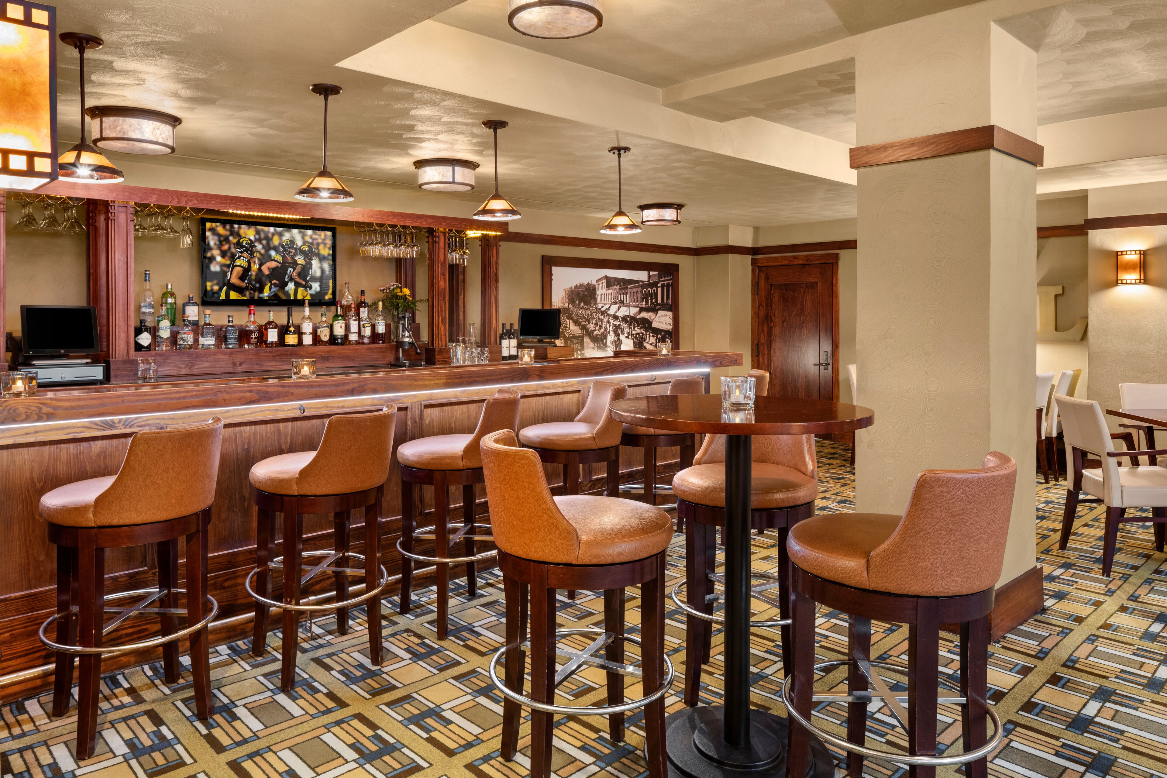 A bar area with wooden stools, a bar counter, and hanging pendant lights.