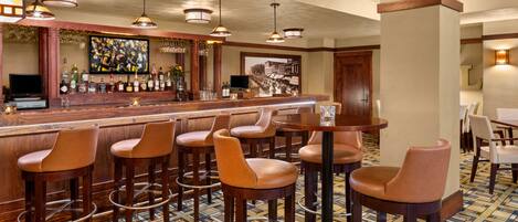 A bar area with wooden stools, a bar counter, and hanging pendant lights.