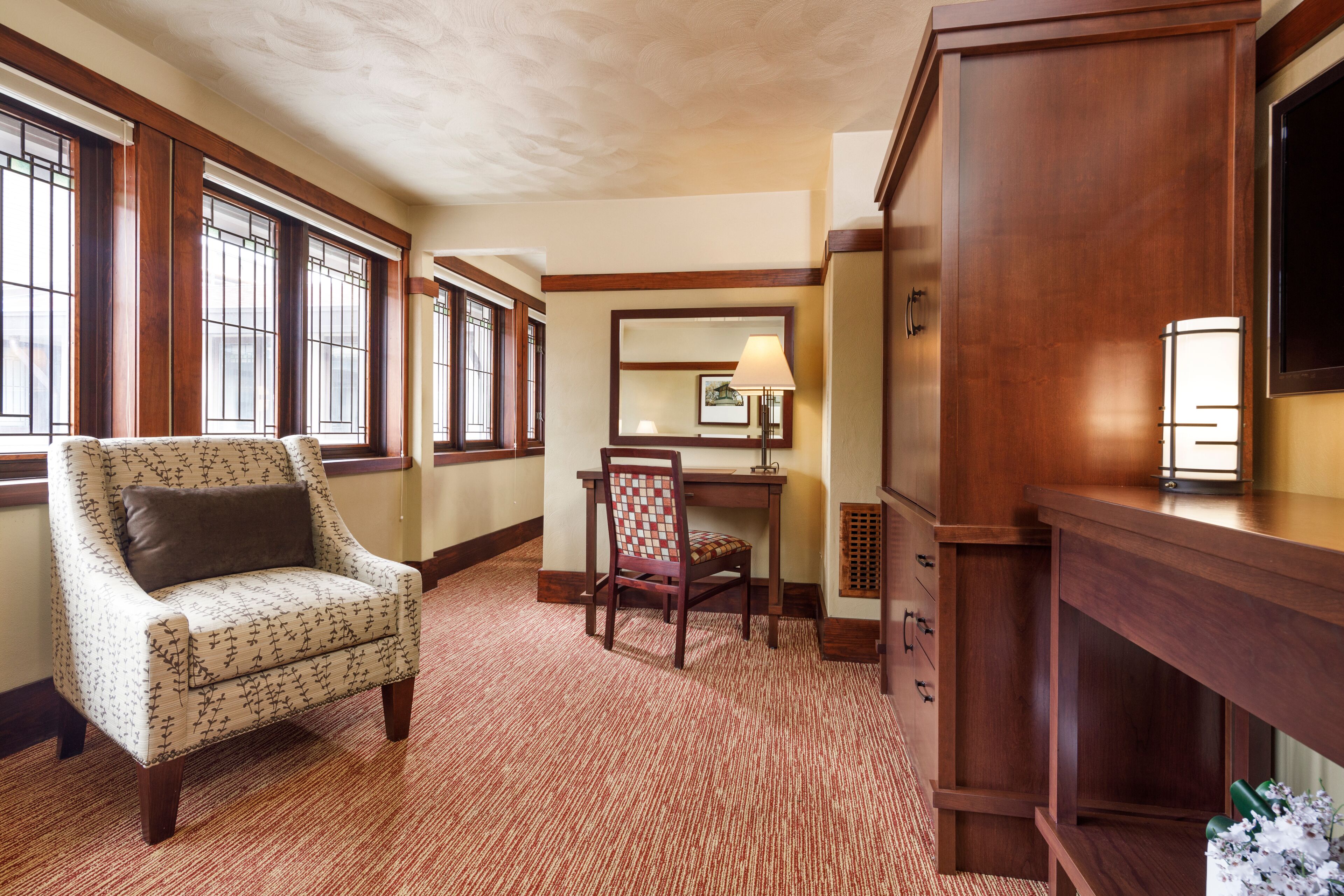 A room with a patterned armchair, a desk, and a large wooden cabinet.