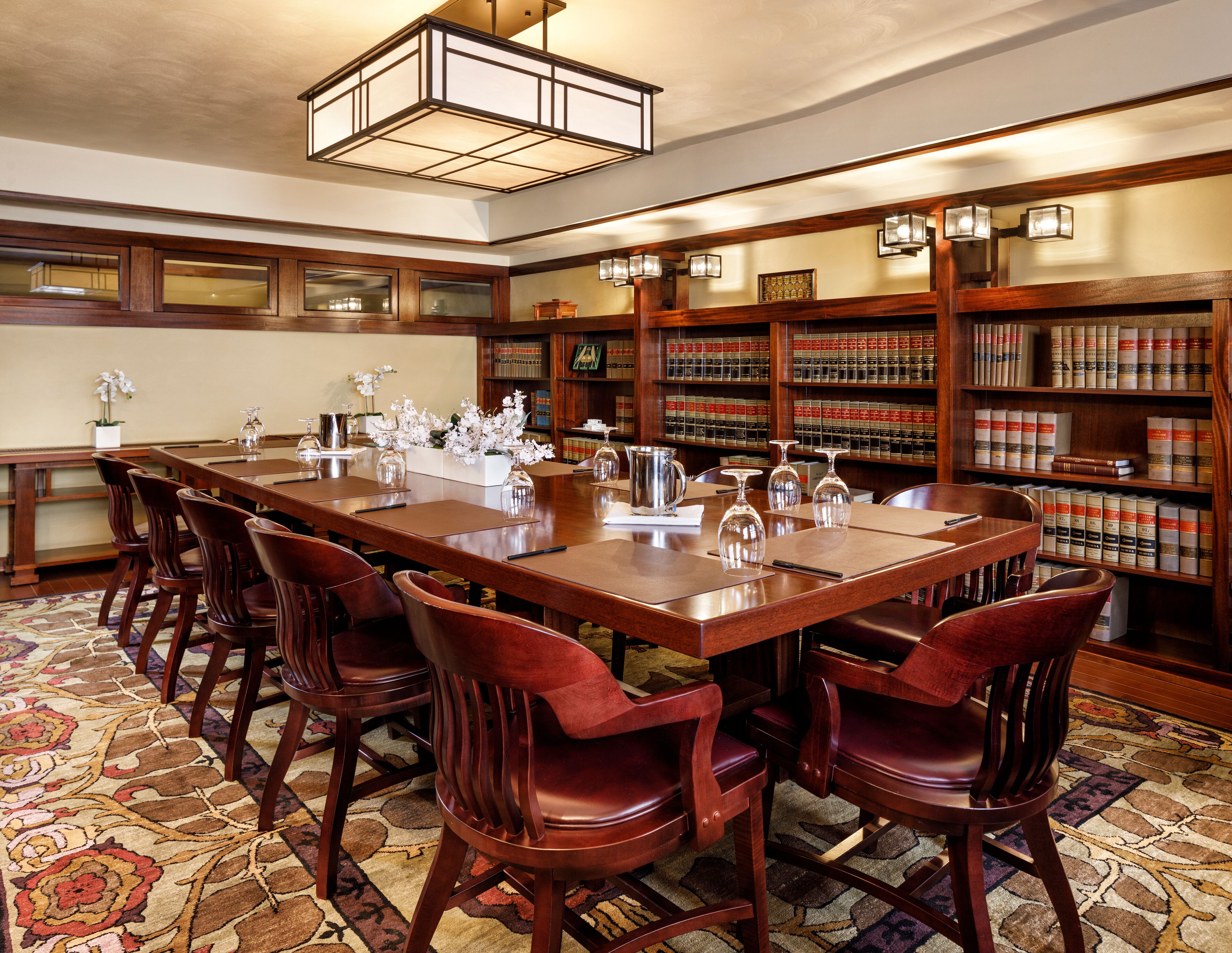 A library with a long wooden table and chairs, surrounded by bookshelves filled with books.