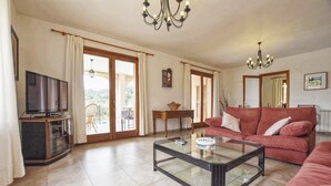 A living room with a television, a glass coffee table, a sofa, and a dining area with a table and chairs. - Holiday Home 'Pla De Ses Rotes' with Mountain View, Wi-Fi and Air Conditioning (Campanet)