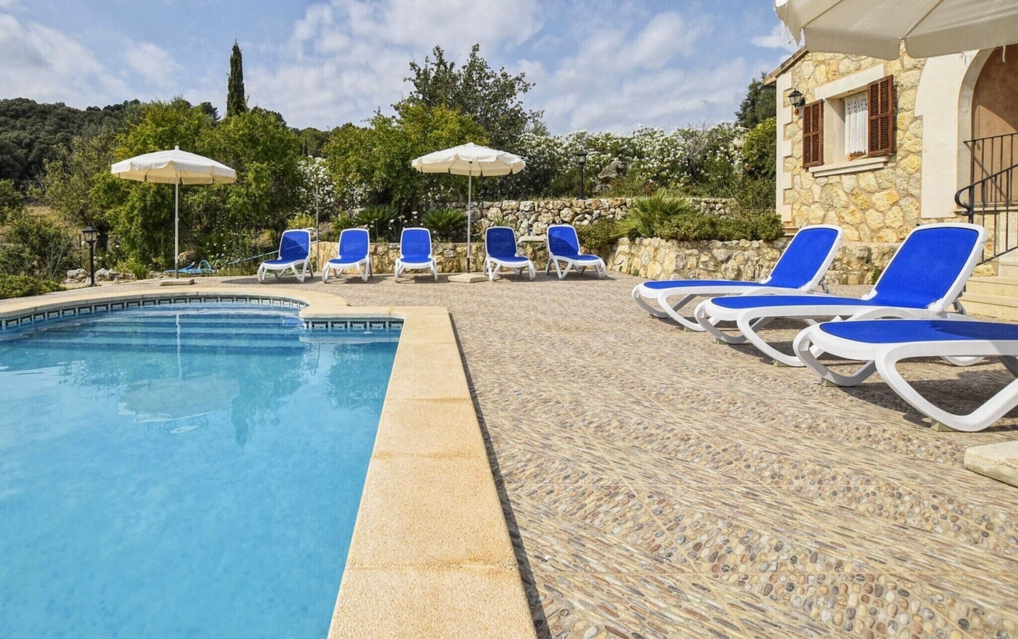 Un área de piscina con sillones de descanso y sombrillas, rodeada de muros de piedra y vegetación.