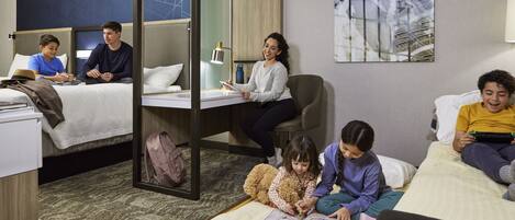 A hotel room with a bunk bed, a desk, and a sofa. There are four people in the room, two adults and two children.