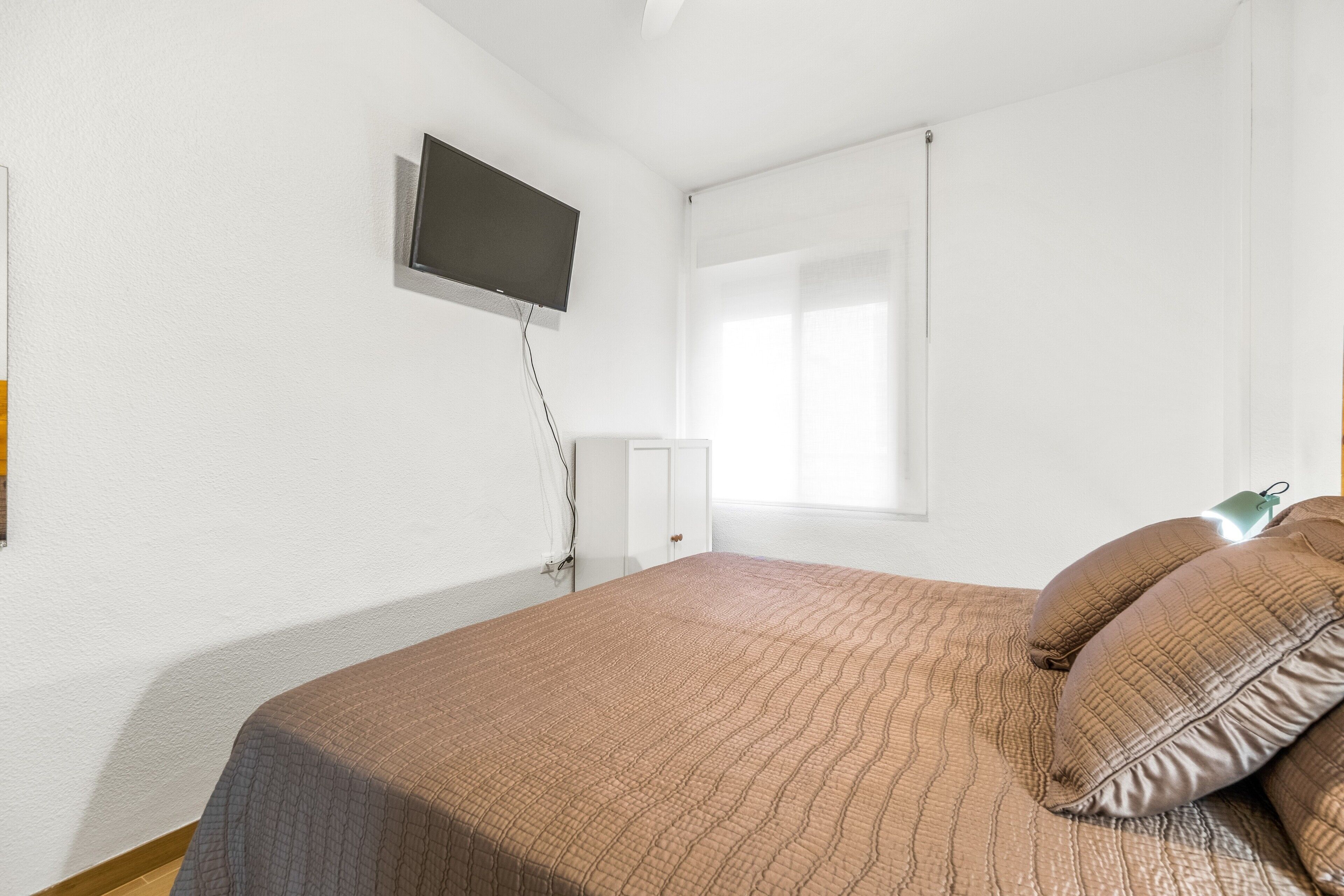 Une chambre à coucher avec un lit, un téléviseur fixé au mur et une fenêtre avec des stores.