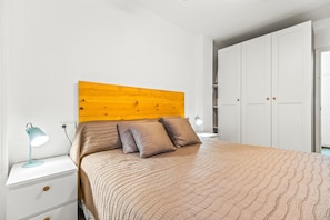 Un dormitorio con cabecera de madera, cama con ropa de cama marrón, mesita de noche con lámpara y armario.