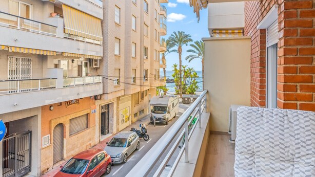 A balcony with a view of a street, a parked van, and a building with a sign. - Apartment 'Moriones Playa' with Balcony, Wi-Fi and Air Conditioning (Torrevieja)
