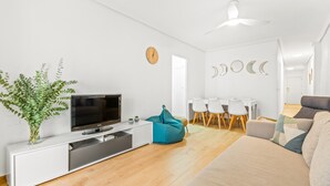 A modern living room with a flat-screen TV, a white sofa, a teal bean bag, a dining area with a white table and chairs, and a ceiling fan. - Apartment 'Moriones Playa' with Balcony, Wi-Fi and Air Conditioning (Torrevieja)