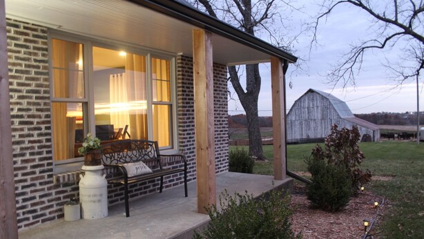 A brick house with a porch, a bench, and a potted plant. - Enjoy rural Missouri and a quiet getaway at White Cottage Farm. (Bogard)