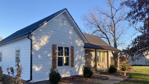 A single-story house with a gabled roof, a front porch with a bench, and a brick exterior. - Enjoy rural Missouri and a quiet getaway at White Cottage Farm. (Bogard)