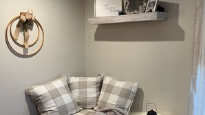 A cozy corner with a round, checkered sofa, a small side table with a lantern, and a wall-mounted shelf with decorative items. - Enjoy rural Missouri and a quiet getaway at White Cottage Farm. (Bogard)