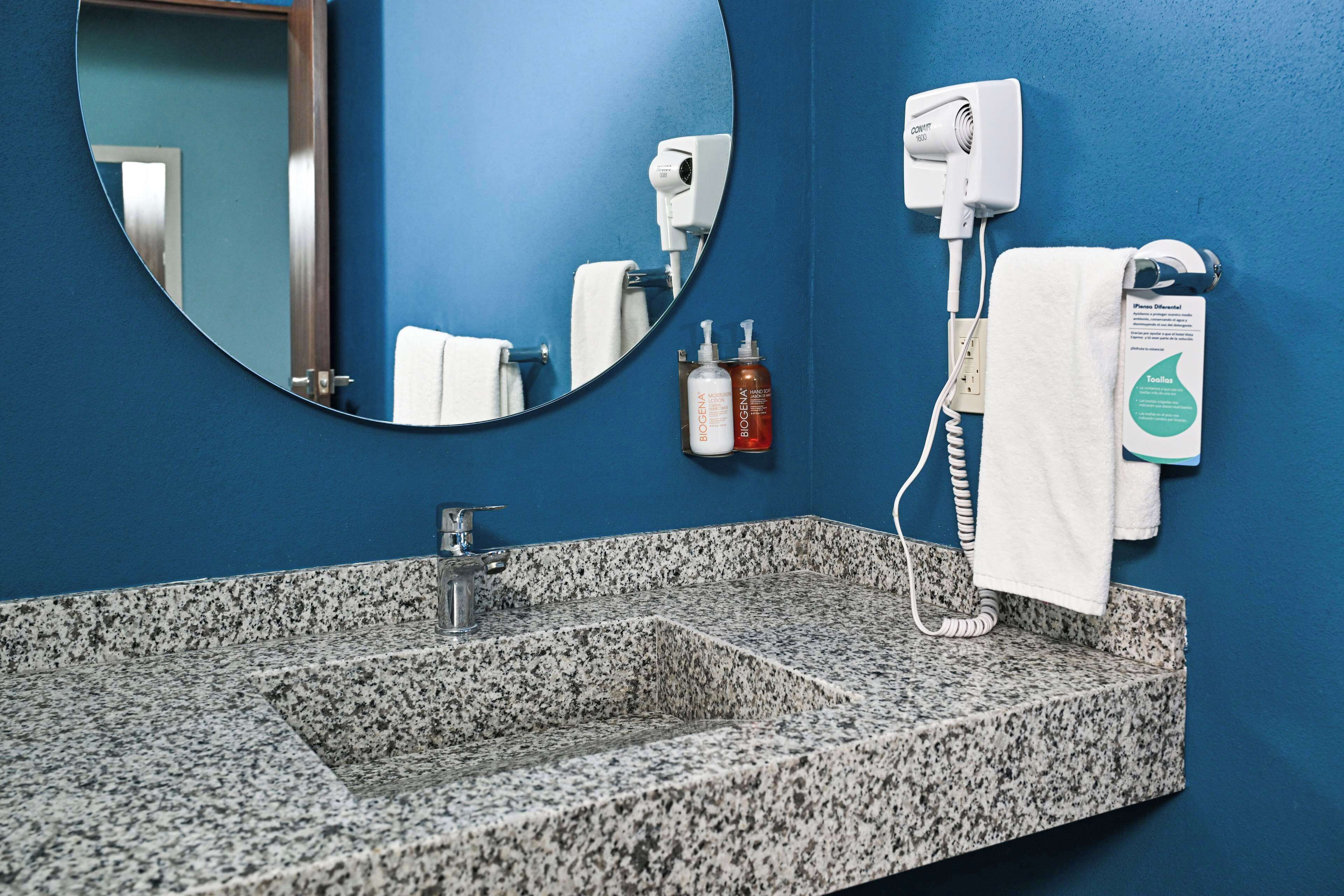 A bathroom with a granite sink, a mirror, a towel rack, and a hairdryer.