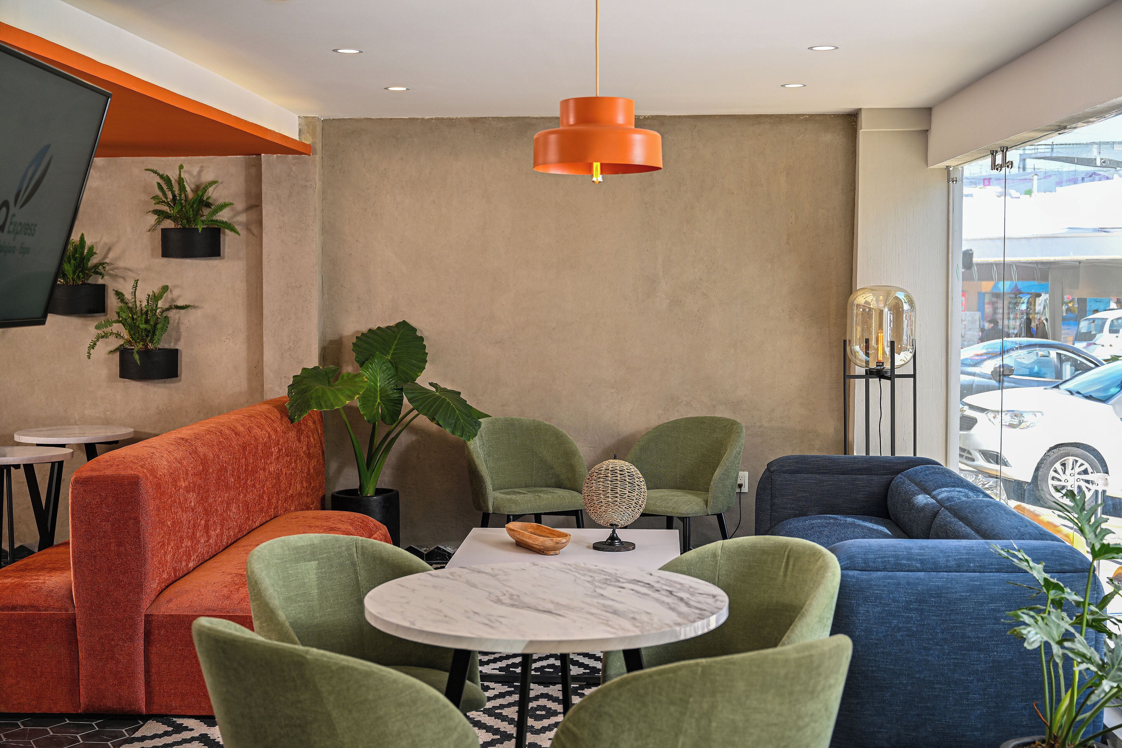 A modern lounge area with a round marble table, green and blue upholstered seating, and a large potted plant.