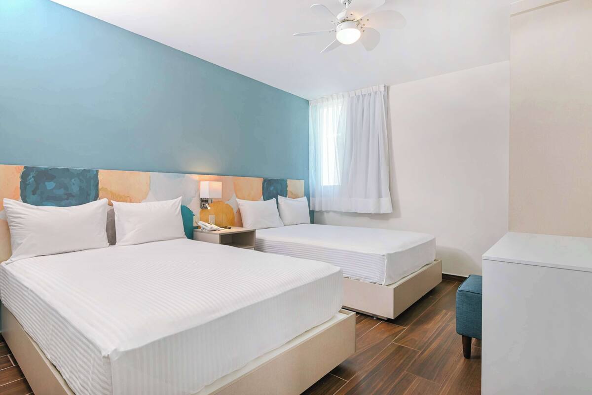 Een hotelkamer met twee bedden, een plafondventilator en een nachtkastje met een lamp.