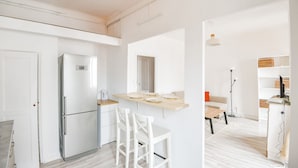 Una cocina moderna con armarios blancos, un refrigerador empotrado y encimera de madera. Hay dos sillas blancas y una mesa de comedor con sillas.