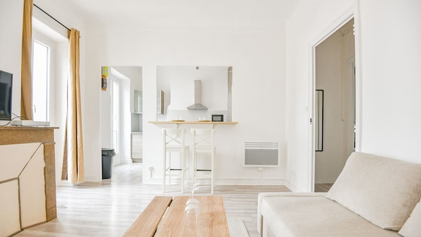 Una sala de estar moderna con una mesa de centro de madera, un sofá color beige y una zona de cocina con armarios blancos y un microondas.
