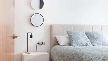 Un dormitorio con cama, dos almohadas, mesita de noche con lámpara y espejo en la pared.