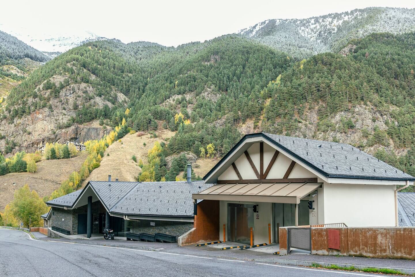 Un bâtiment moderne doté d’un garage et d’une entrée couverte, situé dans un cadre montagneux.