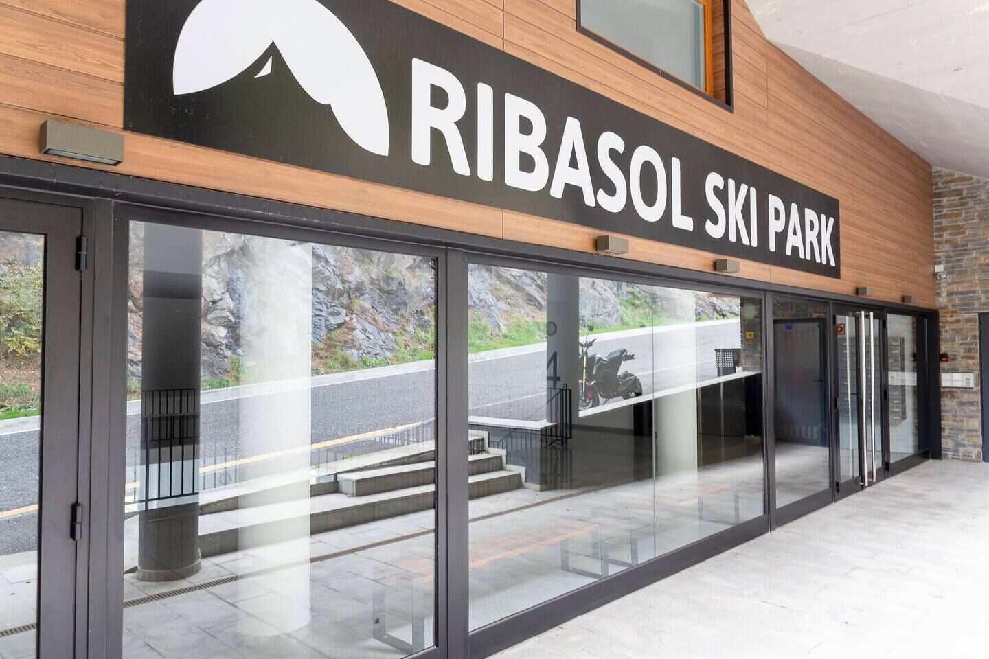 The entrance to Ribasol Ski Park with a large sign, glass doors, and a view of the road outside.