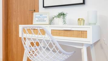 Un bureau blanc avec un panier en osier, un panneau encadré indiquant le mot de passe du réseau Wi-Fi, une petite plante et une bougie.