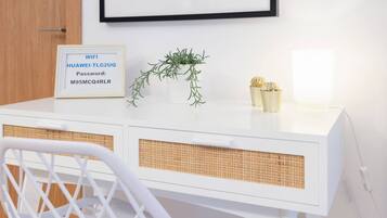 Un escritorio blanco con un cartel del código de acceso WiFi enmarcado, una planta pequeña y dos jarrones decorativos.