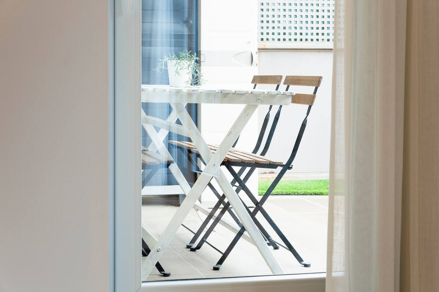 Een witte opklapbare tafel met twee houten stoelen in een lichte, open ruimte.