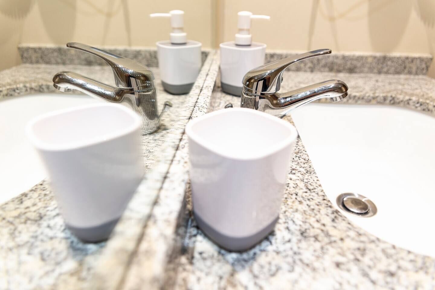 Un baño con encimera de granito, dos lavamanos y dos grifos.