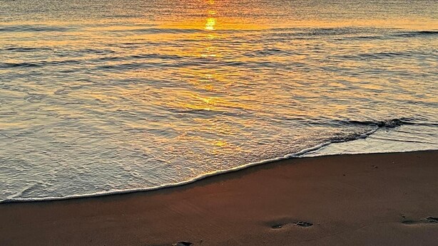 A beach with footprints leading to the water, a sunset over the ocean, and a calm sea. - Completely remodeled 2023 1st Flr Oceanview Emerald Isle,3BR/3BA condo (Emerald Isle)