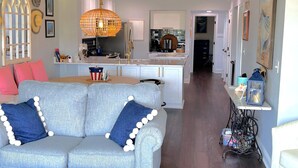 A modern living room with a light blue sofa, a dining area, and a kitchen with white cabinets. - Completely remodeled 2023 1st Flr Oceanview Emerald Isle,3BR/3BA condo (Emerald Isle)