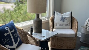 A wicker chair with a cushion and a pillow with an anchor design, a small table with a lamp, and a view of the outdoors. - Completely remodeled 2023 1st Flr Oceanview Emerald Isle,3BR/3BA condo (Emerald Isle)