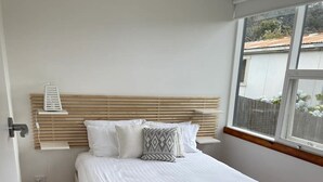 A bedroom with a wooden headboard, white bedding, and a view of the outdoors through a window. - "Jetty's End Bicheno" (Bicheno)